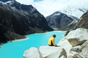 a man sitting on a rock overlooking a mountain lake at Laguna House in Huaraz
