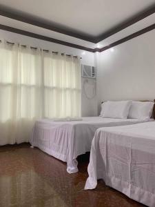 two beds in a white room with white curtains at PEPAYEN INN Homestay in General Luna