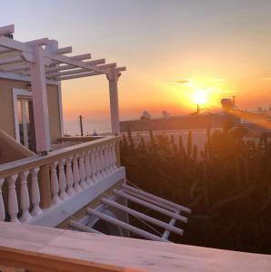 - un coucher de soleil sur une maison avec une terrasse couverte et des escaliers dans l'établissement Danae Villa, à Fira