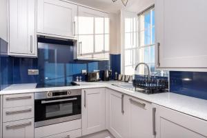 a white kitchen with blue walls and white cabinets at Abbey View in Bath