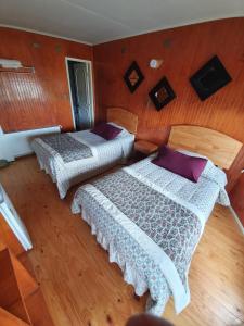 two beds in a bedroom with wooden walls and wooden floors at Hostal Galvarino Puerto Natales in Puerto Natales