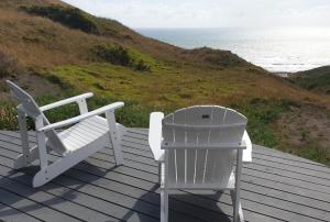 two white chairs sitting on a deck overlooking the ocean at SeaView Retreat -Amazing Ocean Views and Outdoor bath in Waiuku