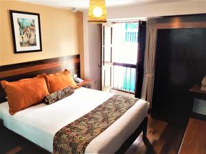 Un dormitorio con una cama con almohadas naranjas y una ventana. en Posada San Blas, en Cusco