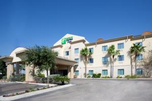 a hotel with palm trees in front of a parking lot at Holiday Inn Express Hotel and Suites Alice, an IHG Hotel in Alice