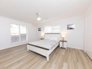 a white bedroom with a bed and two night stands at Tiro Moana in Forster
