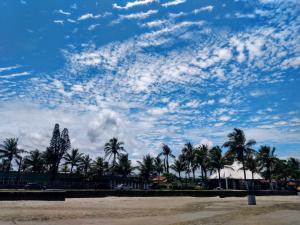 a cloudy sky with palm trees and a beach at Casa linda e confortável a 3 min da praia!!! in Peruíbe
