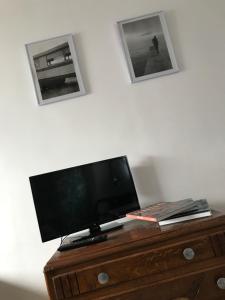 telewizor na drewnianej komodzie z dwoma zdjęciami na ścianie w obiekcie Gite Chez Ginger w mieście Pézenas