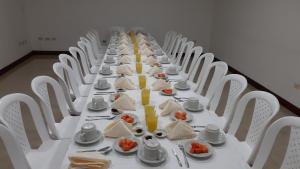 une grande table avec des chaises blanches et des assiettes de nourriture dans l'établissement Hotel Hangas Mayo, à Ipiales