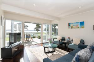 un salon avec un canapé bleu et une télévision dans l'établissement Wairangi Beach Cottage - Paihia Beach House, à Paihia