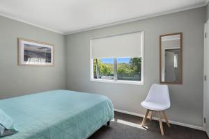 a bedroom with a bed and a chair and a window at Pohutukawa Breeze - Papamoa Beach Holiday Home in Papamoa