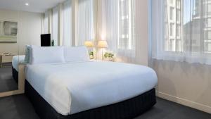 a large white bed in a room with windows at Oaks Melbourne on Collins Suites in Melbourne