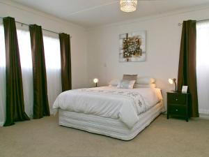 una camera da letto con un letto bianco con tende verdi di Taupo Haven - Taupo Holiday Unit a Taupo