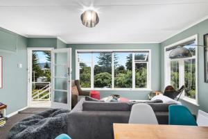 a living room with a gray couch and windows at Seaside House - Waikanae Beach Bach in Waikanae