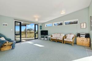 een woonkamer met stoelen en een televisie en een balkon bij The Blue Cottage with WiFi- Waipu Holiday Home in Waipu