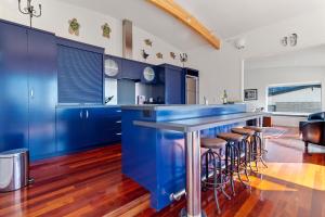 una cocina con armarios azules y un bar con taburetes en Sea Shells By The Shaw - Waihi Beach Holiday Home, en Waihi Beach