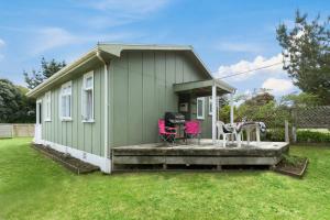 zielony domek z tarasem i różowymi krzesłami w obiekcie The Beach House - Kapiti Coast Holiday Home w mieście Waikanae