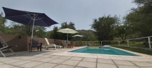 einen Pool mit einem Sonnenschirm und Stühlen sowie einem Tisch und Stühlen in der Unterkunft Complejo de Cabañas Las Abelias in Potrero de los Funes
