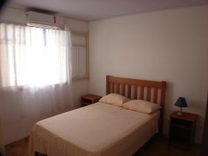1 dormitorio con cama y ventana con colcha blanca en Casa Canasvieiras 250mts praia, en Florianópolis