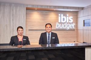 Ein Mann und eine Frau sitzen an einem Schreibtisch in einer Lobby. in der Unterkunft ibis budget Singapore Ruby in Singapur
