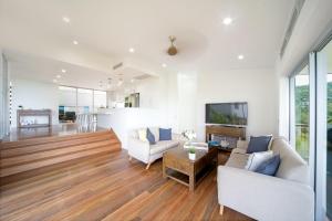 a living room with white furniture and wood floors at Oleander Holiday Home - Airlie Beach in Airlie Beach