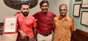 three men are standing next to a table at Hebbar's Heritage Home in Mumbai