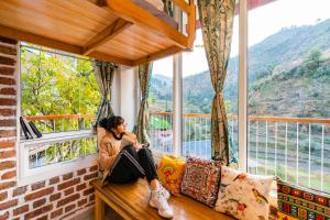 a woman sitting on a couch in a room with a window at Zostel Plus Mussoorie- Kempty in Mussoorie
