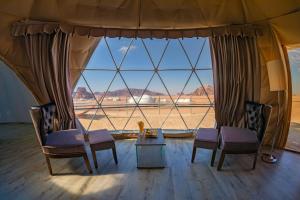 a tent with two chairs and a table in front of a large window at Wadi Rum UFO Luxotel in Wadi Rum