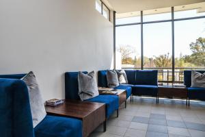 uma sala de espera com sofás azuis e uma mesa e janelas em The Residency Sandhurst em Joanesburgo