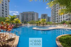 uma grande piscina azul com palmeiras e edifícios em 2 QUARTOS a 200m RIOCENTRO em CONDOMINIO com PISCINA, Estacionamento e Portaria 24h - Area de LAZER tambem para CRIANCAS - Wi-Fi 120mbps e Cozinha Completa no Rio de Janeiro