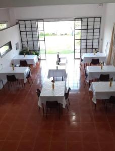 a restaurant with white tables and chairs and windows at Pousada dos Félix in São Gabriel