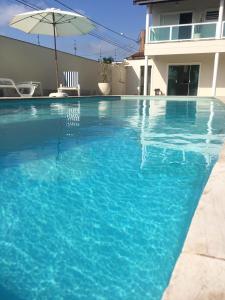 una piscina blu con ombrellone e una casa di Itanhaém Maravilhosa, Bilhar, Sky, WiFi, Piscina e churrasqueira grande, Gramado, Casa linda de alto padrão a 600m praia a Itanhaém