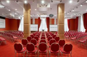 a conference room with red chairs and a podium in the middle at Golden Tulip Rosa Khutor Hotel in Estosadok