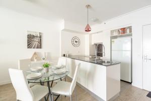 a white kitchen with a glass table and white chairs at Brisbane City Apartments (Tank St CBD) in Brisbane