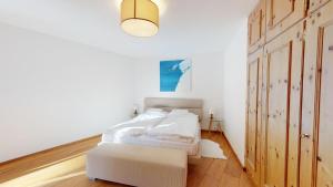 a white bedroom with a white bed and a lamp at La Dmura in Samedan