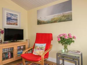 uma sala de estar com uma cadeira vermelha e uma televisão em Tiggy Winkle em Saint Merryn