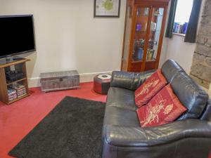 a living room with a leather couch and a flat screen tv at 1 Primitive Mews in Chelmorton