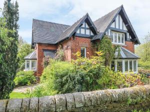 a brick house with a black roof and a stone fence at Gun End Cottage in Rushton Spencer