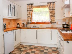 a kitchen with white cabinets and a sink and a window at Little Danescroft in Corpach
