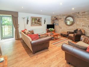 a living room with leather furniture and a stone wall at The Tack Room Cottage in Ashover