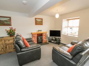 Sala de estar con 2 sofás de cuero y TV en Brickfield Cottage, en Machynlleth