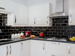 a kitchen with white cabinets and a black tile wall at The Crab Shell in Appledore +9 photos
