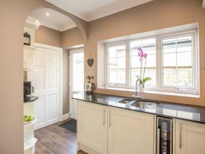 a kitchen with white cabinets and a sink and windows at The Tynemouth Cottage in Tynemouth
