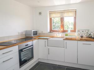 cocina con armarios blancos, fregadero y microondas en Lower West Curry Cottage, en Launceston