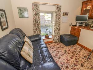 a living room with a leather couch and a television at Sycamore Cottage in Cotterdale