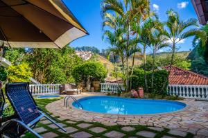 a pool in a yard with two chairs and an umbrella at Hotel Pousada Arcádia Mineira in Ouro Preto