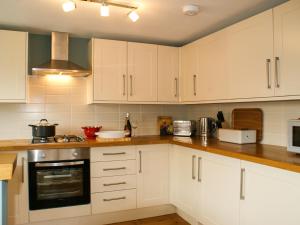 La cuisine est équipée de placards blancs et d'un four avec plaques de cuisson. dans l'établissement Mulberry Cottage, à Hadleigh