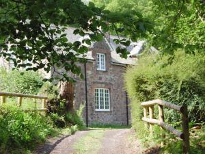 una vieja casa de piedra en un camino de tierra con una valla en Heyden Cottage, en Minehead