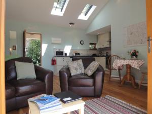 a living room with two leather chairs and a kitchen at 1 Shippen Cottages in Cotleigh