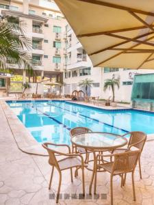 einen Pool mit einem Tisch und Stühlen neben einem Gebäude in der Unterkunft Bombinhas Summer Beach -Apartamento Particular in Bombinhas