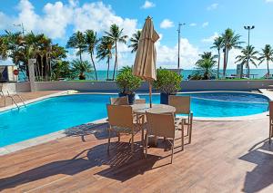 a table and chairs with an umbrella next to a swimming pool at Maceió Mar Hotel in Maceió